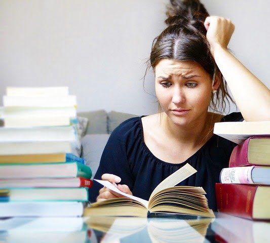 Studerende vrouw aan bureau bezaait met boeken