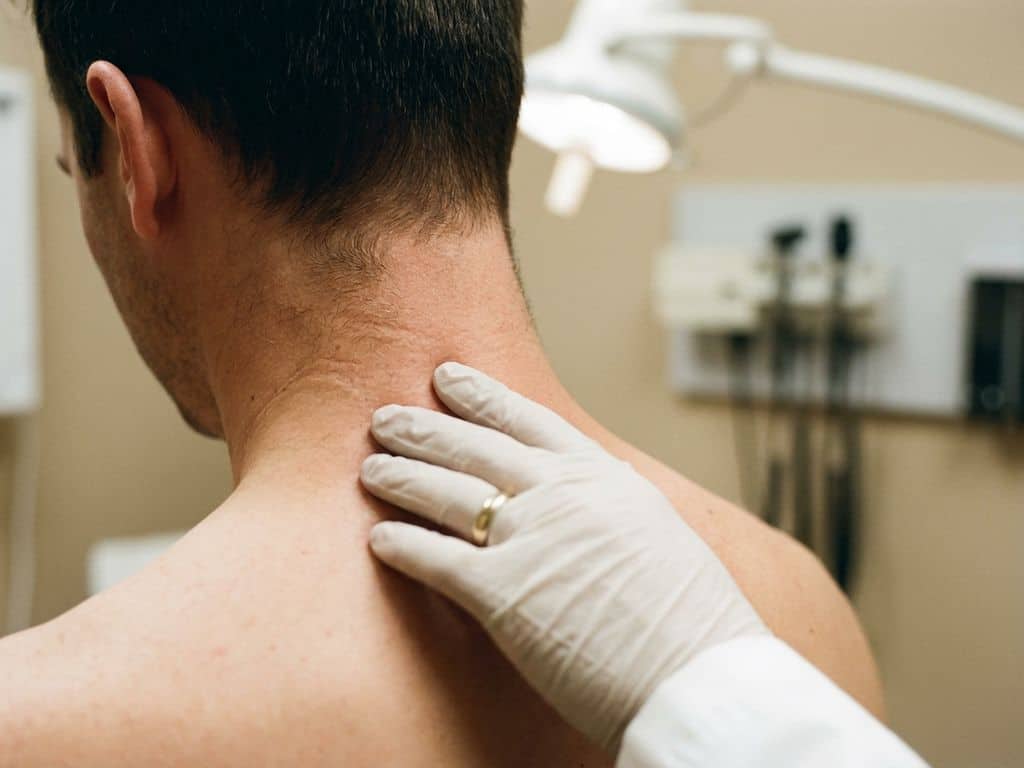Hand drukt zacht op de cervicale wervelkolom nabij C5-C6 tijdens medisch onderzoek, met natuurlijke huidtextuur