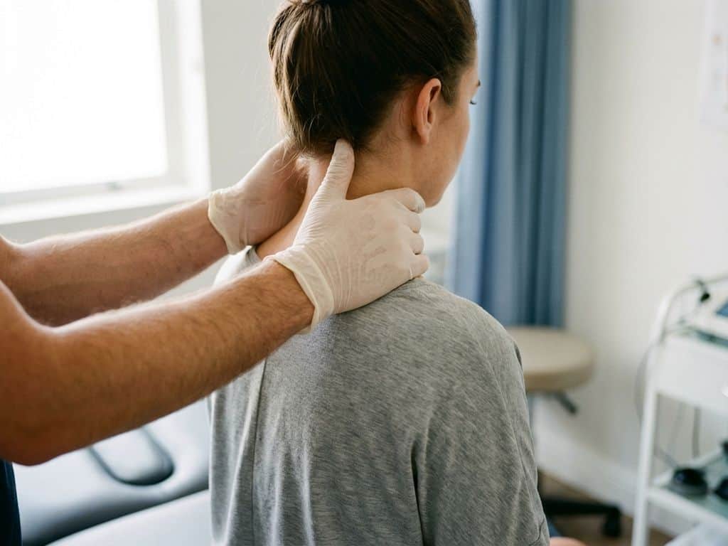 Fysiotherapeut ondersteunt voorzichtig de nek van een patiënt tijdens behandeling in een lichte klinische ruimte