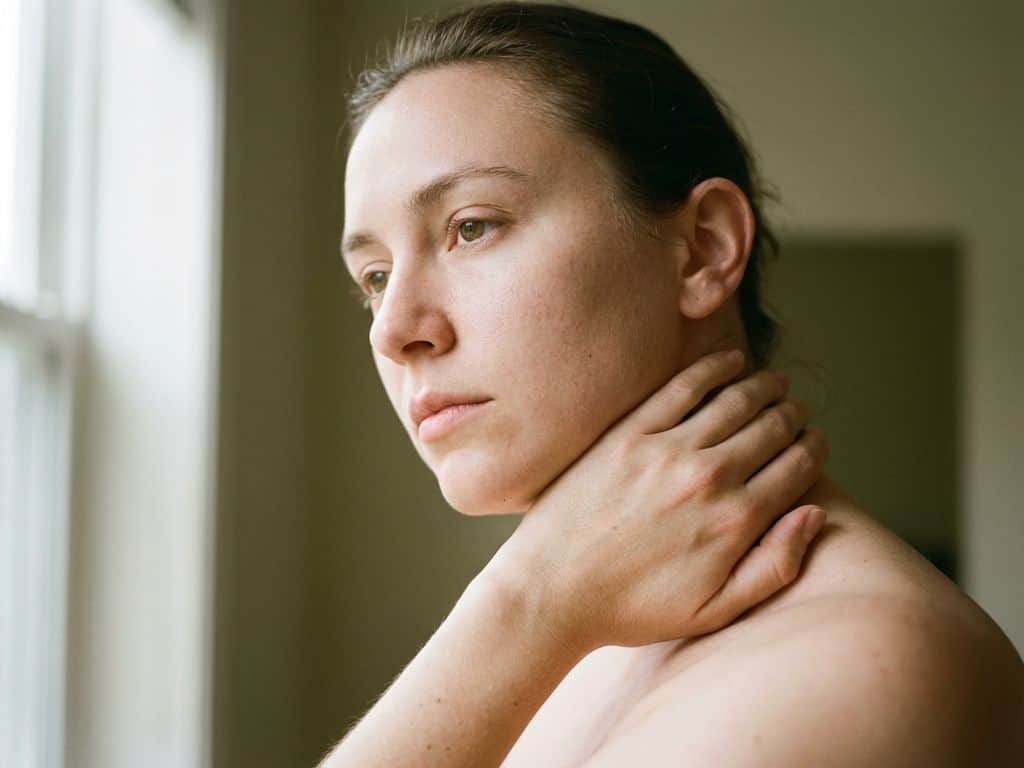 Persoon raakt ontspannen achterkant van nek aan in zacht natuurlijk daglicht, gezonde huid zichtbaar, rustige sfeer